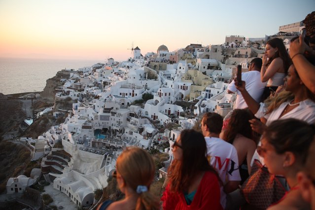 Tourists wait for the sunset in the village of Oia on the Greek island of Santorini on July 20, 2024. Like other popular tourist destinations, the Cycladic island perched on a volcano is approaching over-saturation, and now wants to restrict the number of cruise ships. (Photo by Aris Oikonomou/AFP Photo)