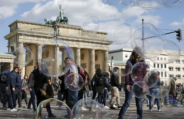 People watch soap bubbles created by a street artist at the Brandenburg Gate in Berlin, Germany, April 20, 2016. (Photo by Fabrizio Bensch/Reuters)