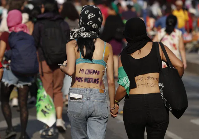 In this March 8, 2019 file photo, women hold hands as they walk with Spanish slogans printed on their backs, reading, from left, “My body, my rules”, and “We are going to tear down (the patriarchy)” during a protest march in Mexico City. The United Nations says that four out of 10 Mexican women will experience sexual violence, such as unwanted groping or rape, during their lifetimes, and that nine women are murdered on average every day in the country. (Photo by Rebecca Blackwell/AP Photo/File)