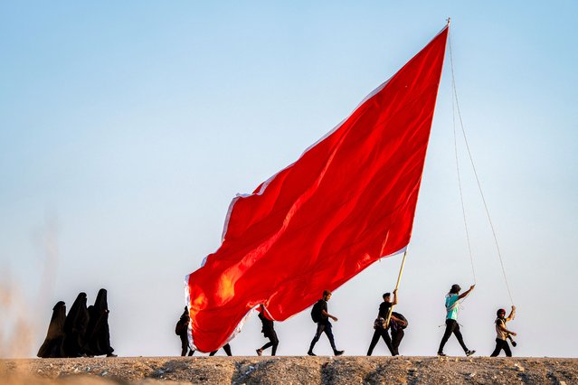 Shiite Muslim pilgrims march with banners towards the shrine city of Karbala ahead of the Arbaeen commemorations that mark the end of the 40-day mourning period for the seventh century killing of the Prophet Mohamed's grandson Imam Hussein ibn Ali, in the city of Nasiriyah in Iraq's southern Dhi Qar province on August 14, 2024. (Photo by Asaad Niazi/AFP Photo)