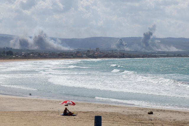 A woman sits on a beach as smoke billows over southern Lebanon following Israeli strikes, amid ongoing cross-border hostilities between Hezbollah and Israeli forces, as seen from Tyre, southern Lebanon on September 23, 2024. (Photo by Aziz Taher/Reuters)