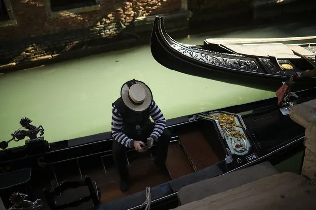 A gondolier looks at his smartphone as he waits for clients in Venice, Italy, Friday, February 28, 2020. Authorities in Italy decided to re-open schools and museums in some of the areas less hard-hit by the coronavirus outbreak in the country which has the most cases outside of Asia, as Italians on Friday yearned for a return to normal life even amid fears that the outbreak could plunge the country's economy into recession. (Photo by Francisco Seco/AP Photo)