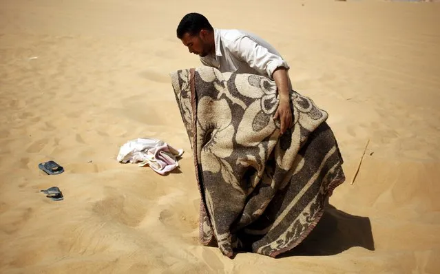 A worker helps a patient, who is wrapped in a blanket, leave a “sauna” tent after his sand bath in Siwa, Egypt, August 12, 2015. In the searing heat of summer in western Egypt, at the hottest time of the day, sufferers of rheumatism, joint pain, infertility or impotence lie buried neck-deep in the sand of Siwa near Dakrour Mountain. (Photo by Asmaa Waguih/Reuters)