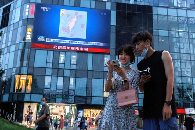 People stand in front of a screen showing a CCTV news broadcast, featuring a map of locations around Taiwan where Chinese People's Liberation Army (PLA) will conduct military exercises and training activities including live-fire drills, at a shopping center in Beijing, China on August 3, 2022. (Photo by Thomas Peter/Reuters)