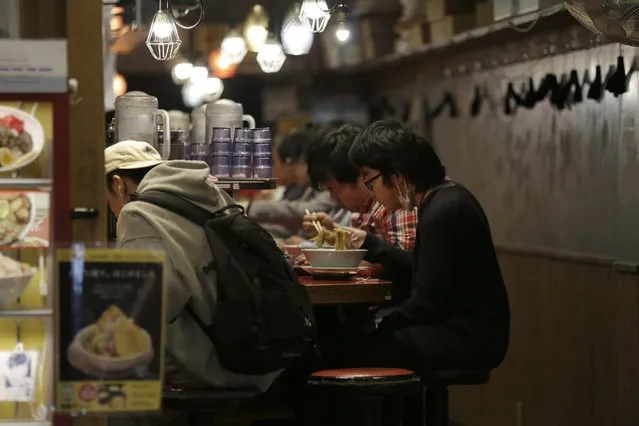 In this April 25, 2020, photo, people eat at a small ramen shop in the entertainment district near Shibuya station right before the 8pm government requested closing time for restaurants and bars in Tokyo. Under Japan's coronavirus state of emergency, people have been asked to stay home. Many are not. Some still have to commute to their jobs despite risks of infection, while others are dining out, picnicking in parks and crowding into grocery stores with scant regard for social distancing. (Photo by Kiichiro Sato/AP Photo)