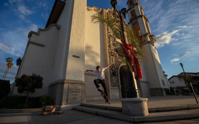 Miles de Rouin, an art student at San Francisco State, jumps on his skateboard outside St. Charles Borromeo Church, which was decorated with the Stations of the Cross, in Los Angeles on Friday, April 10, 2020. Churches in the state were closed due to the coronavirus. (Photo by Damian Dovarganes/AP Photo)