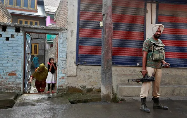 A girl peers from her house as a member of the security forces patrols a street in Srinagar as the city remains under curfew following weeks of violence in Kashmir August 19, 2016. (Photo by Cathal McNaughton/Reuters)