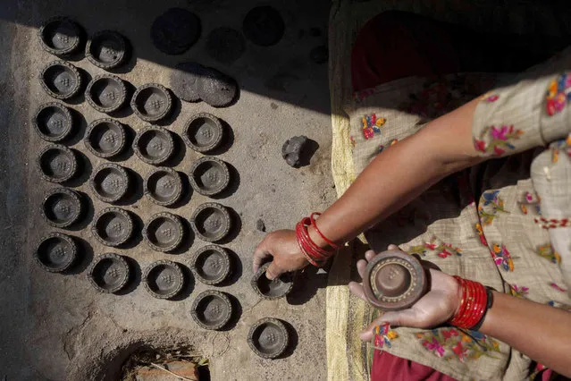 A potter makes earthen lamps for the upcoming Tihar festival in Bhaktapur, Nepal, Friday, October 21, 2022. During the five-day festival, also known as Yama panchak and similar to the Indian festival of Diwali, Hindus decorate their houses and worship Lakshmi, the goddess of wealth, and various animals like the crow, dog, cow and ox during the festival of lights. (Photo by Niranjan Shrestha/AP Photo)