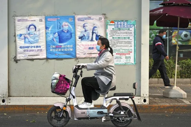 A woman rides past a coronavirus testing facility displaying posters promoting the COVID-19 vaccination in Beijing, Wednesday, October 26, 2022. (Photo by Andy Wong/AP Photo)