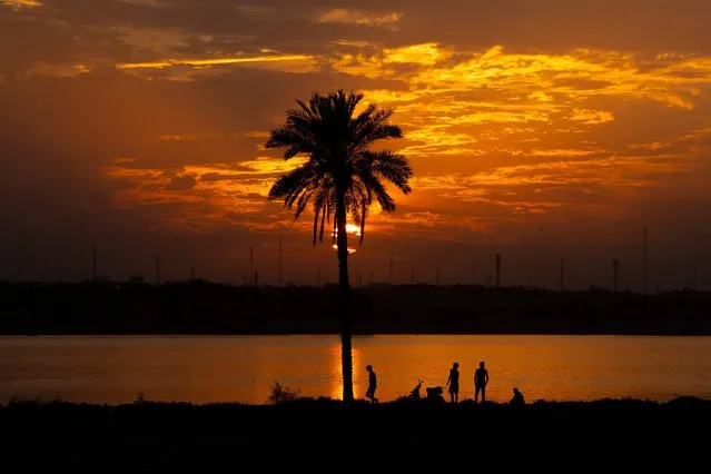 Iraqis stand on the shore of the Shatt al-Arab waterway, formed at the confluence of the Euphrates and Tigris rivers, as the sun sets over Iraq's southern city of Basra on October 30, 2022. (Photo by Hussein Faleh/AFP Photo)