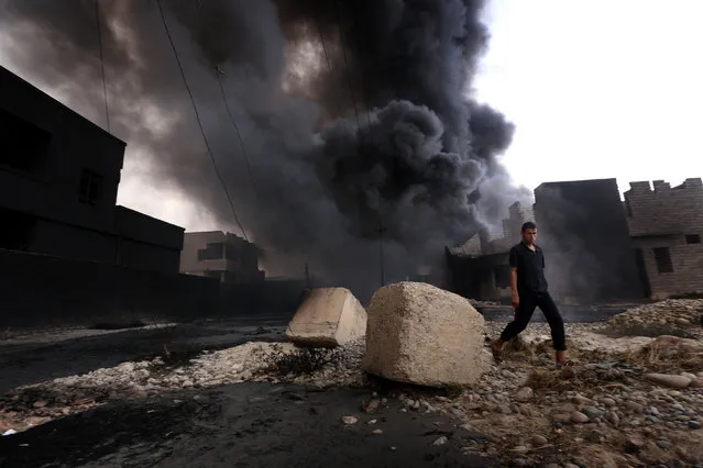An Iraqi man walks near smoke billowing from oil wells, set ablaze by Islamic State (IS) group militants before fleeing the oil-producing region of Qayyarah, on August 30, 2016, after Iraqi forces pushed the jihadists out of the northern town on the banks of the Tigris river. Iraqi forces on August 25 retook key areas in the city and pushed the Islamic State group from Qayyarah, a northern town considered strategic for any future offensive against the jihadists' last stronghold of Mosul. (Photo by Safin Hamed/AFP Photo)
