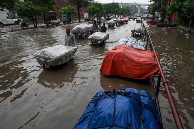 Street vendors pull their carts protected with tarpaulin as they wade through a flooded street after heavy monsoon rains in Lahore on July 16, 2020. (Photo by Arif Ali/AFP Photo)