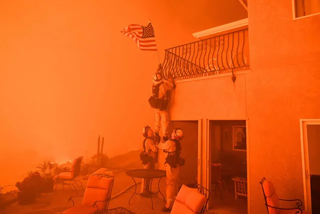 Firefighters remove a US flag as flames from the “Wall Fire” close in on a luxury home in Oroville, California on July 8, 2017. The first major wildfires after the end of California's five-year drought raged across the state on July 8, as it was gripped by a record-breaking heatwave. (Photo by Josh Edelson/AFP Photo)