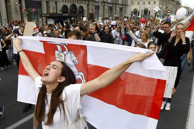 A woman reacts as she marches holding an old Belarusian national flag in the center of Minsk, Belarus, Friday, August 14, 2020. Some thousands of people have flooded the cnetre of the Belarus capital, Minsk, in a show of anger over a brutal police crackdown this week on peaceful protesters that followed a disputed election. (Photo by Sergei Grits/AP Photo)