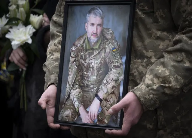 A Ukrainian serviceman holds the photo of his comrade during the funeral ceremony of Volodymyr Yezhov killed in a battlefield with Russian forces at St. Volodymyr Cathedral in Kyiv, Ukraine, Tuesday, December 27, 2022. Yezhov was a game designer in the development of the game Cossacks 2. He was also one of the authors of the game S.T.A.L.K.E.R.: Clear Sky. Yezhov was also one of the most famous Ukrainian e-sportsmen – played StarCraft under the nickname Fresh. Since the Russian invasion, Volodymyr Yezhov went to the frontline and fought as part of the volunteer squadron. (Photo by Efrem Lukatsky/AP Photo)