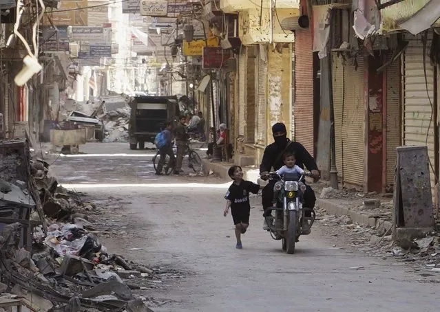 A free Syrian Army fighter rides a motorcycle with a child as a boy runs beside them on a street in Deir al-Zor April  3, 2013. (Photo by Khalil Ashawi/Reuters)