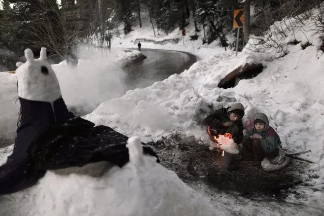 Pakistani Anwar Ali, 13, center, and his brother Hamad, 8, sit around a fire to warm themselves from the cold, while waiting for customers to pose for a picture next to a snow statue they built on a roadside, in Murree, near Islamabad, Pakistan, Wednesday, January 9, 2013. (Photo by Muhammed Muheisen/AP Photo)
