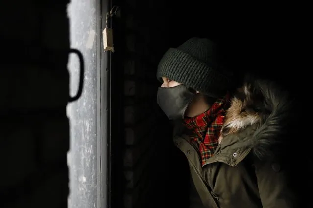 A young demonstrator wearing a face mask to help curb the spread of the coronavirus looks out of a dark garage where he is hiding from the police during an opposition rally to protest the official presidential election results in Minsk, Belarus, Sunday, December 13, 2020. (Photo by AP Photo/Stringer)