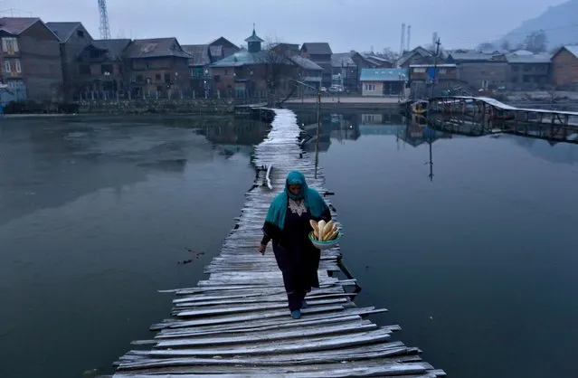 A woman carries bread as she walks on a frost-covered footbridge in the interiors of Nigeen Lake on a cold winter morning in Srinagar, December 24, 2020. (Photo by Danish Ismail/Reuters)