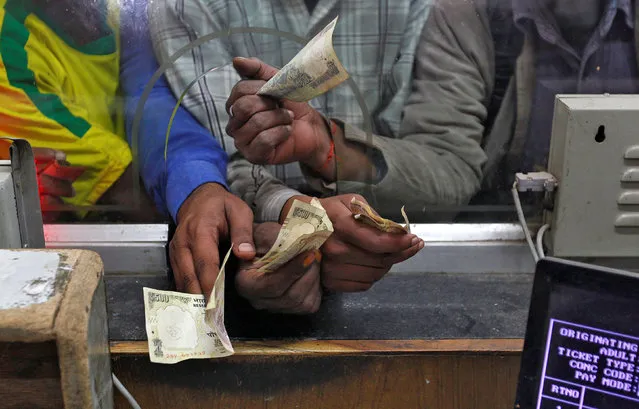 Passengers hold 500 (bottom) rupee banknotes to buy train tickets at a railway booking counter in Allahabad, India, November 9, 2016. (Photo by Jitendra Prakash/Reuters)