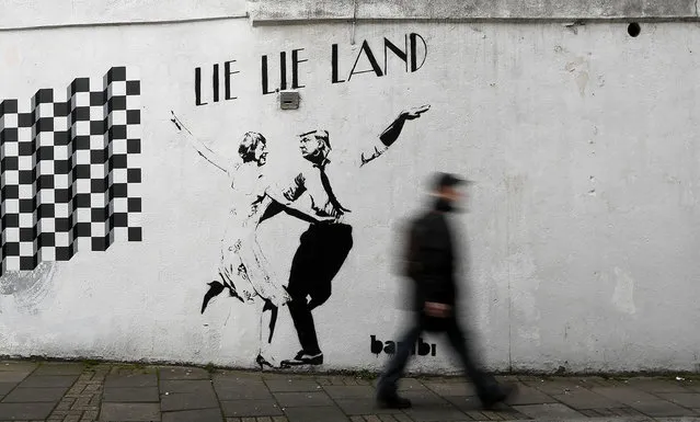 A pedestrian passes a new piece of art by street artist Bambi in London. in London, February 16, 2017. The work, entitled Lie Lie Land, features a dancing British Prime Minister Theresa May and President Donald Trump in the pose made famous by the movie La La Land. (Photo by Kirsty Wigglesworth/AP Photo)