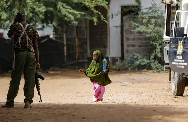 A Somali refugee girl walks past an armed Kenyan policemen outside a field hospital of the International Rescue Committee (IRC) at the Dadaab refugee camp in northern Kenya Friday, July 14, 2023. One of the world's largest refugee camps offers a stark example of the global food security crisis with thousands of people fleeing Somalia in recent months to escape drought and extremism but finding little to eat when they arrive at the Dadaab camp in neighboring Kenya. (Photo by Brian Inganga/AP Photo)