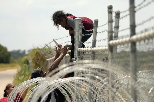 Migrants who crossed the Rio Grande from Mexico into the U.S. climb a fence with barbed wire and concertina wire, Monday, August 21, 2023, in Eagle Pass, Texas. (Photo by Eric Gay/AP Photo)
