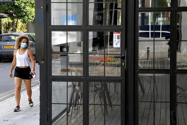 A woman wearing protective face mask walks outside of a closed cafe amid COVID-19 pandemic restrictions government in central capital Nicosia, Cyprus, Thursday, May 6, 2021. Cyprus has unveiled a phased rollback of COVID-19 lockdown restrictions over the next month including a shortened curfew and a reopening of all schools next week, but will enforce the compulsory display of proof of vaccination, virus testing or convalescence from the disease in areas were people gather in numbers, including restaurants and churches. (Photo by Petros Karadjias/AP Photo)