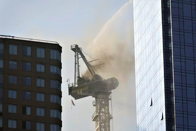 Smoke rises from a construction crane that caught fire, lost its long arm, which smashed against a nearby building, dangled and then plummeted to the street as people ran for their lives on the sidewalk below in Manhattan, Wednesday, July 26, 2023, in New York. (Photo by Seth Wenig/AP Photo)