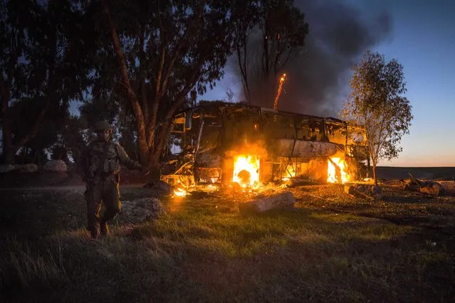 An Israeli soldier stands near a burning bus after it was hit by a mortar shell fired from Gaza near the Israel Gaza border, Monday, November 12, 2018. Israel's military says it is prepared to step up its efforts against Palestinian militants in the Gaza Strip if rocket fire at Israel continues. (Photo by Tsafrir Abayov/AP Photo)