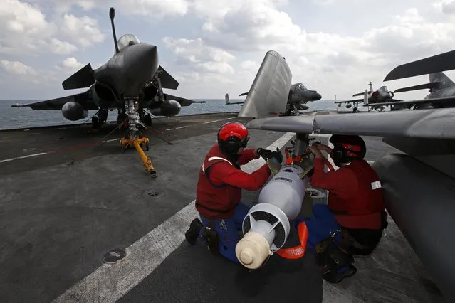 Red jacket ordnance crew equip a Super Etendard fighter jet near a Rafale fighter jet aboard France's Charles de Gaulle aircraft carrier in the Gulf, January 29, 2016. (Photo by Philippe Wojazer/Reuters)