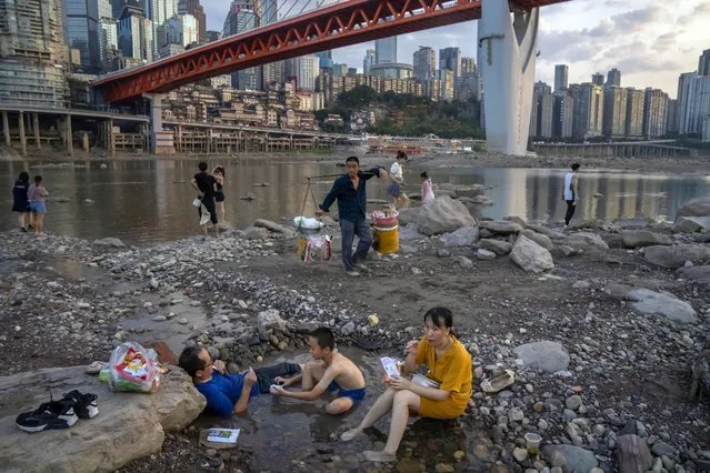 People sit in a shallow pool of water in the riverbed of the Jialing River, a tributary of the Yangtze, in southwestern China's Chongqing Municipality, Saturday, August 20, 2022. The very landscape of Chongqing, a megacity that also takes in surrounding farmland and steep and picturesque mountains, has been transformed by an unusually long and intense heat wave and an accompanying drought. (Photo by Mark Schiefelbein/AP Photo)
