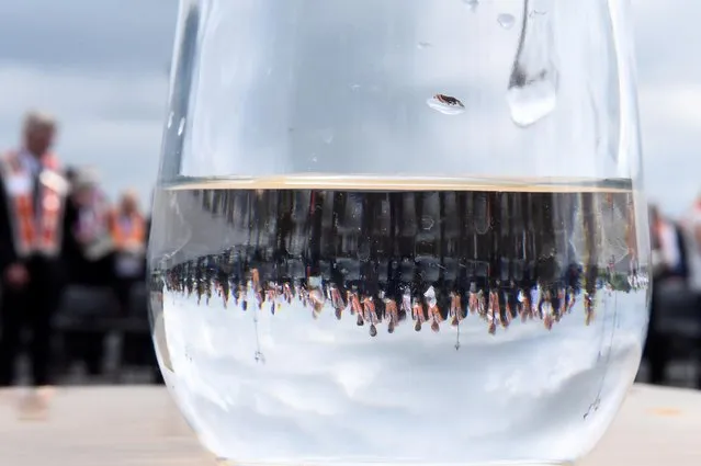 Participants in a Loyalist Orange Order parade are seen reflected in a glass of water in Portadown, Northern Ireland on July 4, 2021. (Photo by Clodagh Kilcoyne/Reuters)