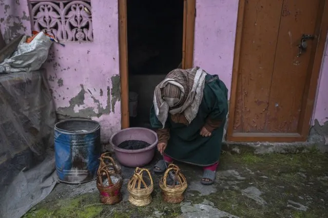 A Kashmiri woman fills a traditional firepot called Kangri with charcoal in Srinagar, Indian controlled Kashmir, Friday, January 5, 2024. Kangri is an age old device for keeping warm, consisting of a decoratively woven yellow wicker case housing an earthen pot for burning charcoal. Even the modern day heating gadgets have failed to replace it, mainly due to its portability and low cost. (Photo by Dar Yasin/AP Photo)
