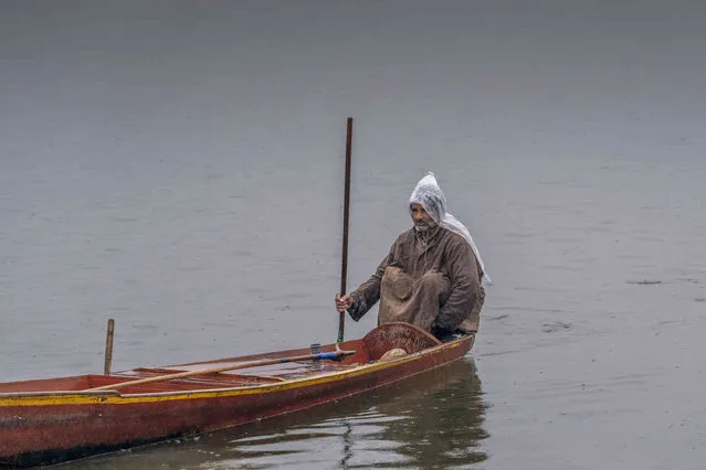 A Kashmiri fisherman wraps his head with a plastic sheet as he rows a shikara, or traditional boat, in the rain on Dal Lake in Srinagar, Indian controlled Kashmir, Saturday, March 2, 2024. (Photo by Dar Yasin/AP Photo)
