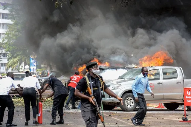 People extinguish fire on cars caused by a bomb explosion near Parliament building in Kampala, Uganda, on November 16, 2021. Two explosions hit Uganda's capital Kampala on November 16, 2021, injuring a number of people in what police termed an attack on the city, the latest in a string of blasts targeting the country. The explosions occurred in the central business district of Kampala near the central police station and the entrance to parliament, police said. (Photo by Ivan Kabuye/AFP Photo)