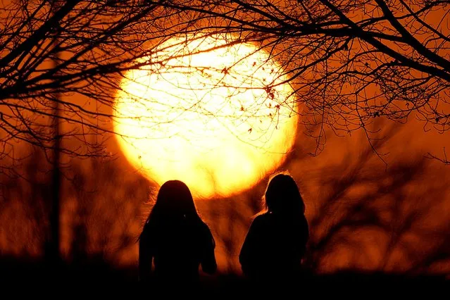 People watch the sunset at a park on an unseasonably warm day, Sunday, February 25, 2024, in Kansas City, Mo. A warm front is sweeping springlike weather across a large swath of the country in what is usually one of the coldest months of the year. (Photo by Charlie Riedel/AP Photo)