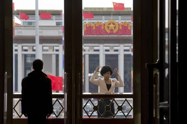 A television presenter adjusts her hair near a security person guarding the entrance to the Great Hall of the People where the closing ceremony of the Chinese People's Political Consultative Conference is held in Beijing, China, Wednesday, March 12, 2014. (Photo by Ng Han Guan/AP Photo)