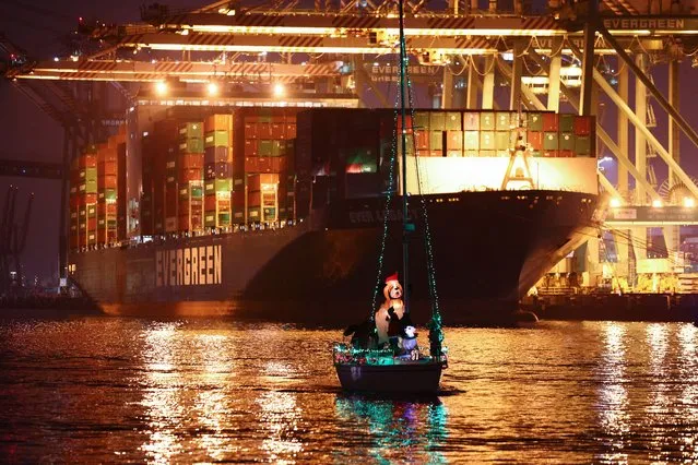 A holiday themed boat parades past a container ship at the Port of Los Angeles during the “Los Angeles Harbor Holiday Afloat Parade” on December 4, 2021 in San Pedro, California. The 59th annual boat parade marking the start of the holiday season featured boats of various sizes competing for awards. A backlog of aging cargo at the ports of Los Angeles and Long Beach has decreased 37 percent since last month. (Photo by Mario Tama/Getty Images)