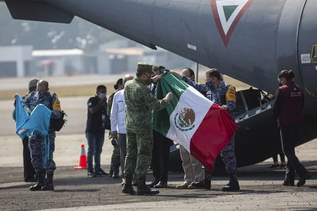 Members of the Mexican Armed Forces unfold a Mexican national flag next to the plane transporting the remains of Guatemalan migrants killed in a truck crash in southern Mexico, on the tarmac of La Aurora International Airport in Guatemala City, Thursday, December 30, 2021. Fifteen more Guatemalan victims of the Dec. 9 migrant smuggling accident that left 56 migrants dead were returned to Guatemala Thursday for burial. (Photo by Oliver de Ros/AP Photo)