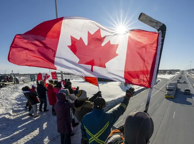 Supporters wave flags on an overpass in Kanata, Ontario, Canada, as a trucker convoy making it's way to Parliament Hill in Ottawa to participate in a cross-country truck convoy protesting measures taken by authorities to curb the spread of COVID-19 and vaccine mandates passes by on Saturday, January 29, 2022. (Photo by Frank Gunn/The Canadian Press via AP Photo)