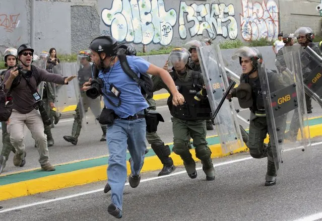 Reuters photojournalist Marco Bello runs as Venezuelan National Guard soldiers chase him during a protest outside the Supreme Court in Caracas, Venezuela, Friday, March 31, 2017. Security forces violently repressed small protests that broke out in Venezuela's capital Friday after the government-stacked Supreme Court gutted congress of its last vestiges of power, drawing widespread condemnation from foreign governments. (Photo by Ariana Cubillos/AP Photo)