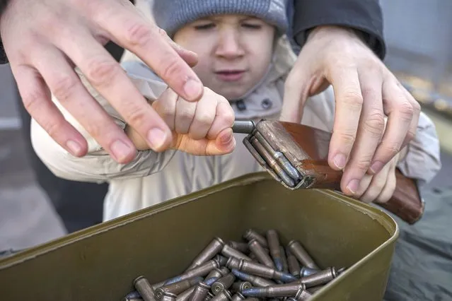 A small child struggles to remove ammunition from a clip during a basic combat training for civilians, organized by the Special Forces Unit Azov, of Ukraine's National Guard, in Mariupol, Donetsk region, eastern Ukraine, Sunday, February 13, 2022. (Photo by Vadim Ghirda/AP Photo)