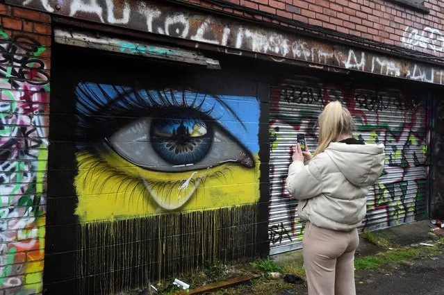 A woman takes a picture of a mural of a weeping eye in the colors of the Ukrainian flag by artist MyDogSighs, in Cardiff, Wales, Britain on March 2, 2022. (Photo by Rebecca Naden/Reuters)