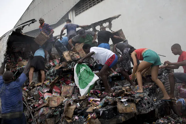People climb onto a cargo truck looking to salvage what merchandise they can after firefighters extinguished the cargo truck allegedly set on fire by drug traffickers, in Rio de Janeiro, Brazil, Tuesday, May 2, 2017. Several public buses and cargo trucks were torched in Rio de Janeiro on Tuesday in what Brazilian military police said was likely gang retaliation for a large anti-drug operation. (Photo by Silvia Izquierdo/AP Photo)