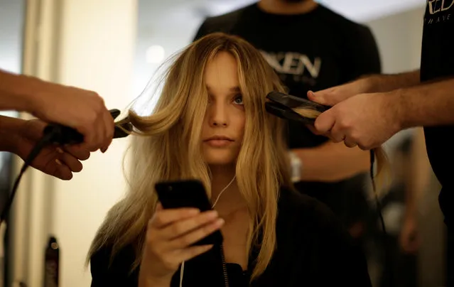 A model looks up from her mobile phone as stylists work on her hair before a show by Australian fashion house Albus Lumen at Fashion Week Australia in Sydney on May 15, 2017. (Photo by Jason Reed/Reuters)