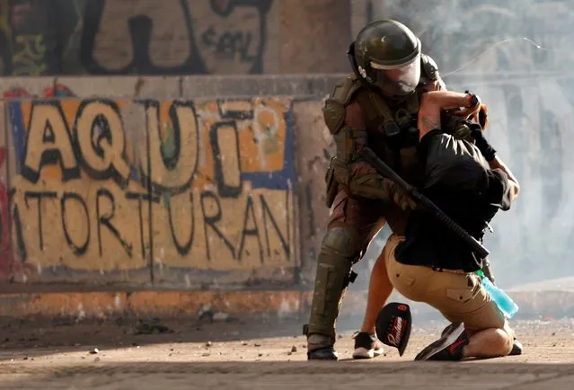 A police officer detains a demonstrator during a protest against Chile's government in Santiago, Chile on November 5, 2019. The graffiti on the wall reads “Here they torture”. (Photo by Jorge Silva/Reuters)
