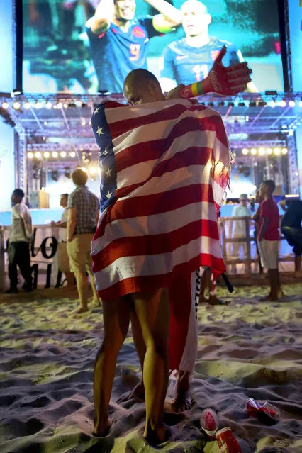 A couple embraces with the American flag wrapped around them as they watch the football game featuring Spain vs. Netherland on the giant screen showing the match at the FIFA World Cup Fan Fest on Copacabana beach on June 13, 2014 in Rio de Janeiro, Brazil. The match was played on the second day of the World Cup tournament and Spain lost 5-1. (Photo by Joe Raedle/Getty Images)