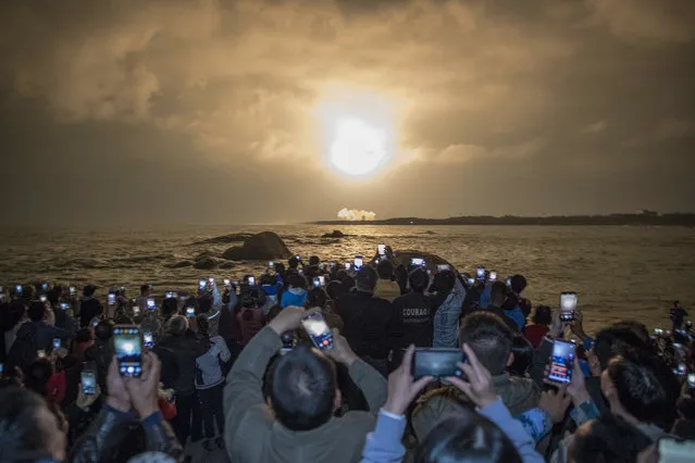 People take photos as China's heavy-lift Long March 5 rocket blasts off from its launch centre in Wenchang, south China's Hainan province on December 27, 2019. China on December 27 launched one of the world's most powerful rockets in a major step forward for its planned mission to Mars in 2020. (Photo by AFP Photo/China Stringer Network)