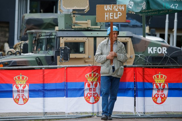 A person holds a placard as members of the NATO-led Kosovo Force (KFOR) stand guard outside municipal offices in Leposavic, Kosovo on June 2, 2023. (Photo by Ognen Teofilovski/Reuters)